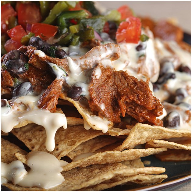 Close up of nachos with cheese sauce, pulled meat, and beans